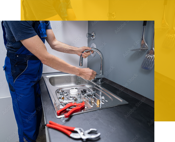 Plumber in blue overalls repairing a kitchen sink, with tools on the countertop.