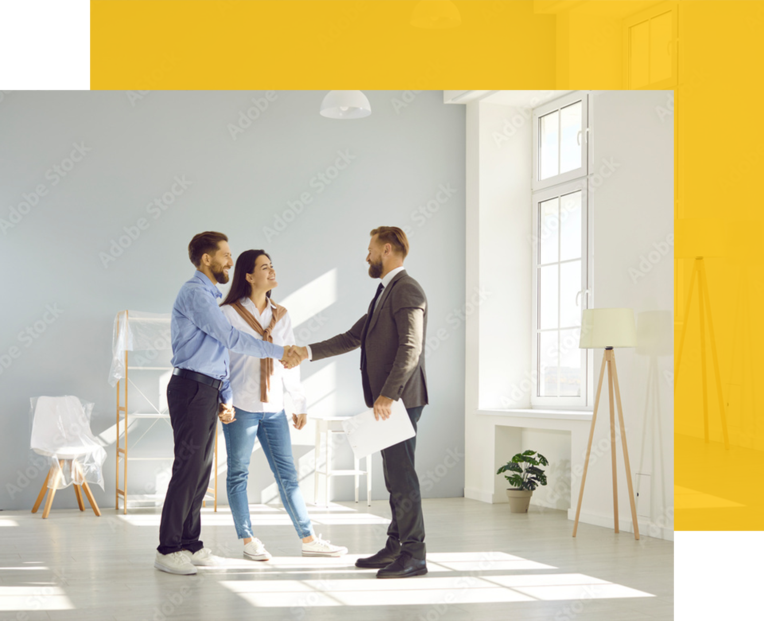 Couple shaking hands with a real estate agent in an empty apartment.