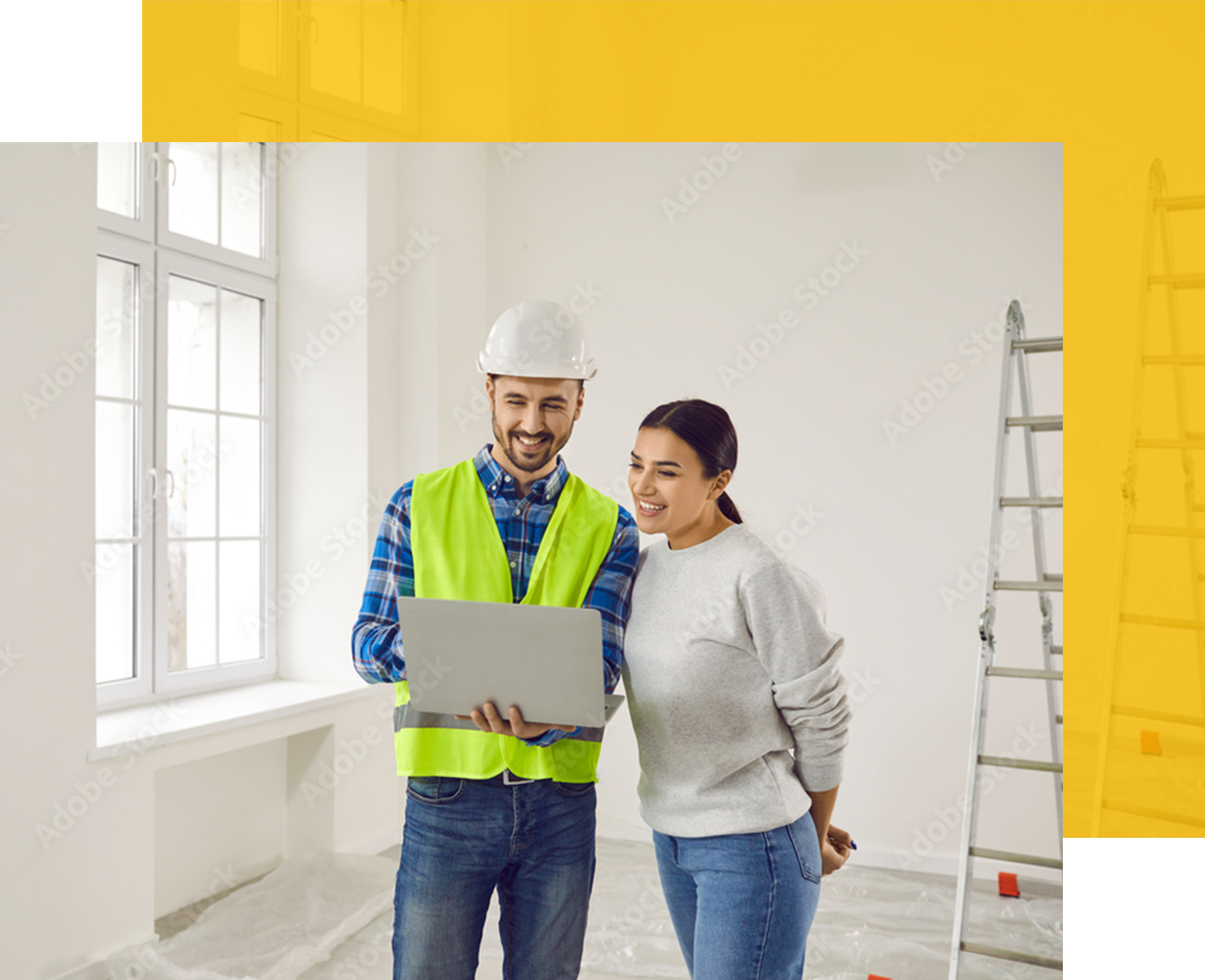 Construction worker in hard hat and a woman looking at a laptop in a room under renovation.