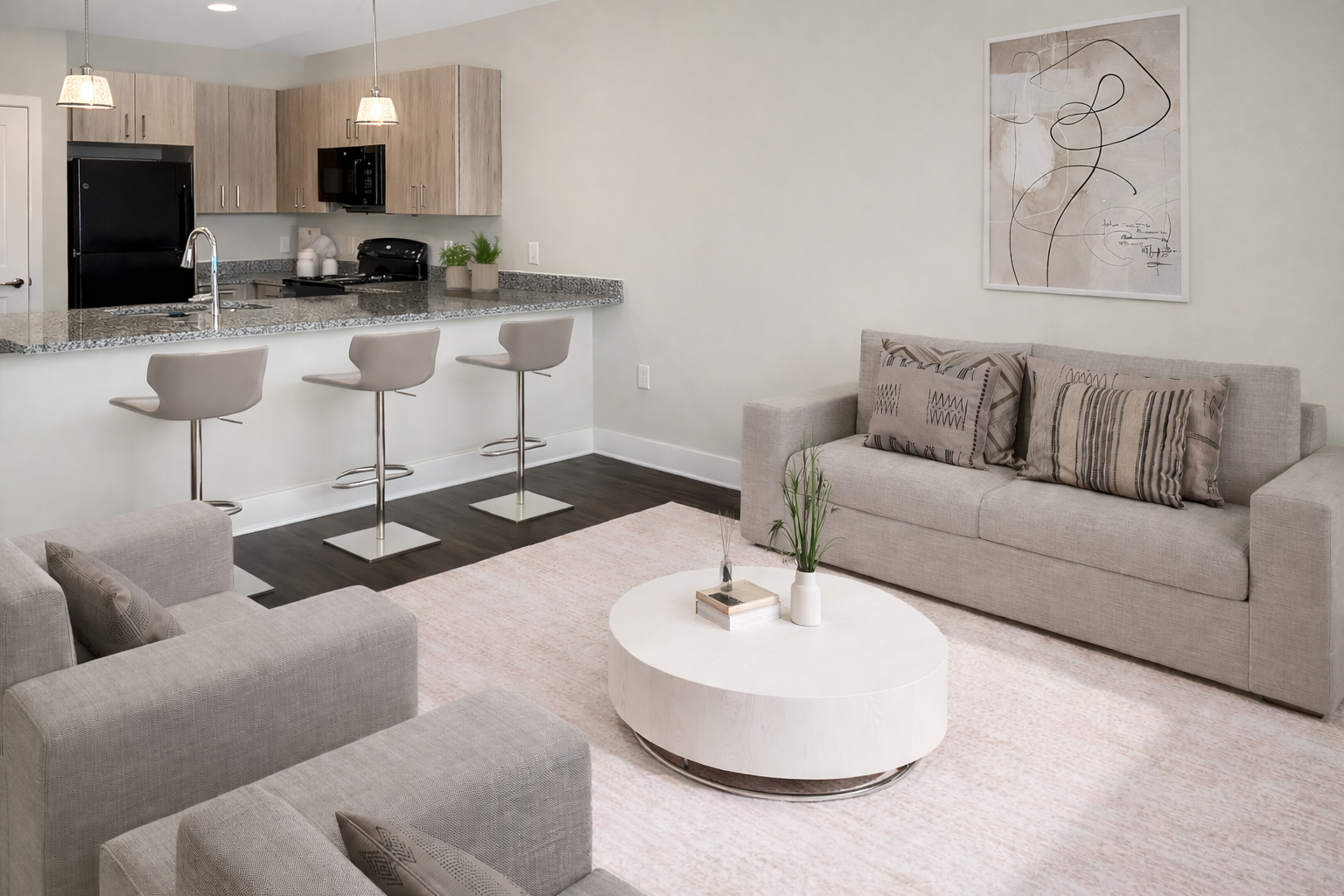 Open-concept living area with a kitchen island, three bar stools, and gray couches.