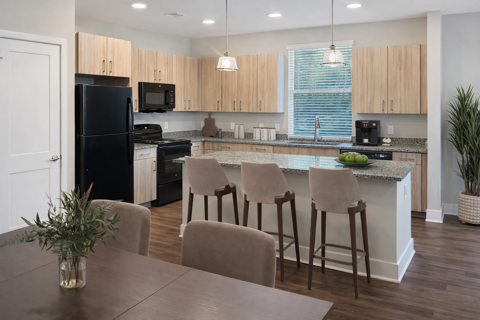 Modern apartment kitchen with granite counters, an island, and light wood cabinets.