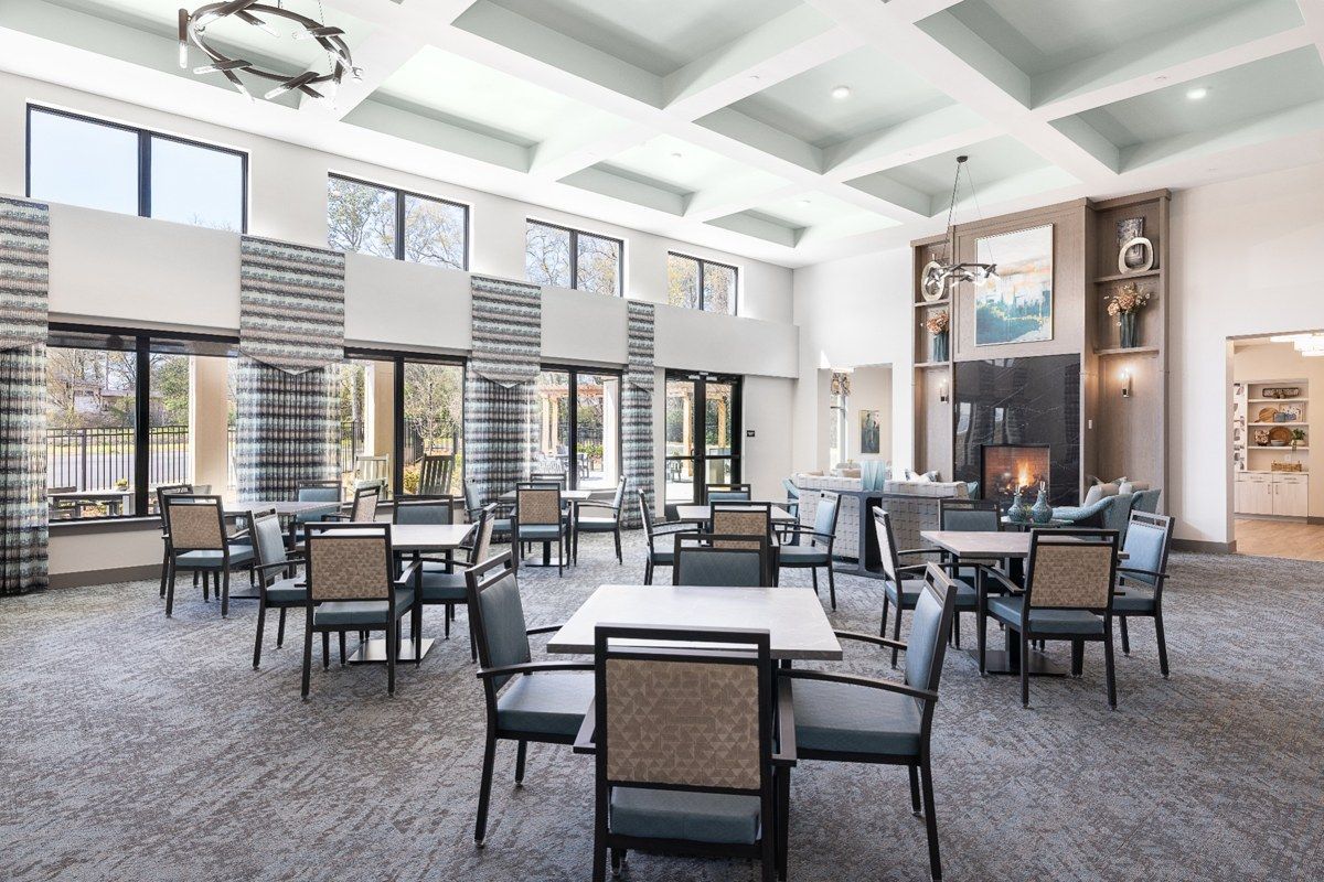 Bright modern dining room with tables, chairs, large windows, and a high coffered ceiling.