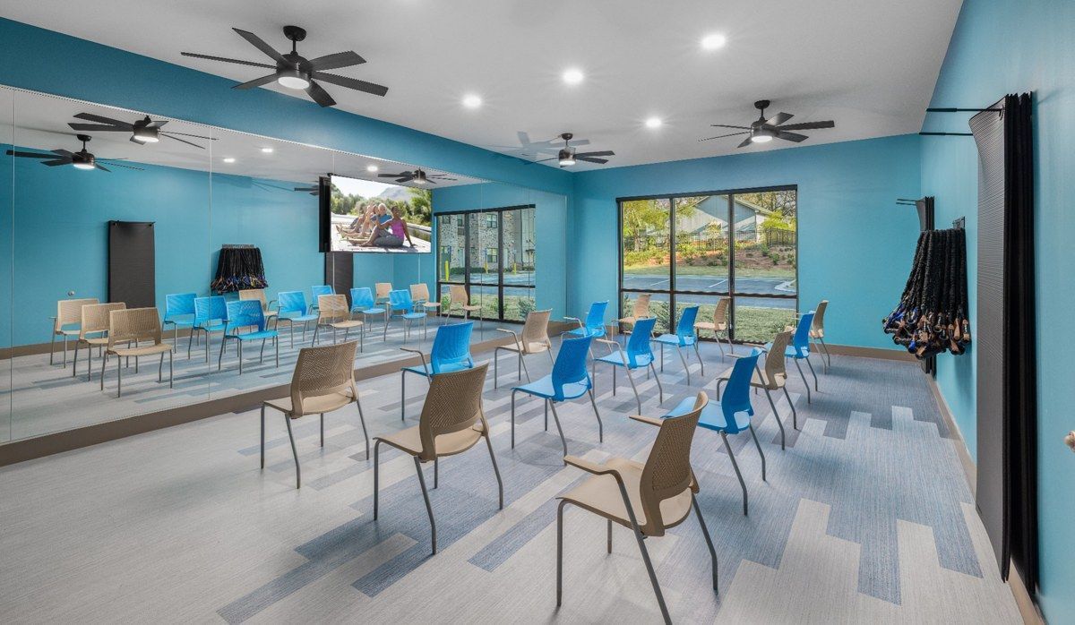 Bright meeting room with rows of blue and beige chairs, wall mirror, ceiling fans, and large windows