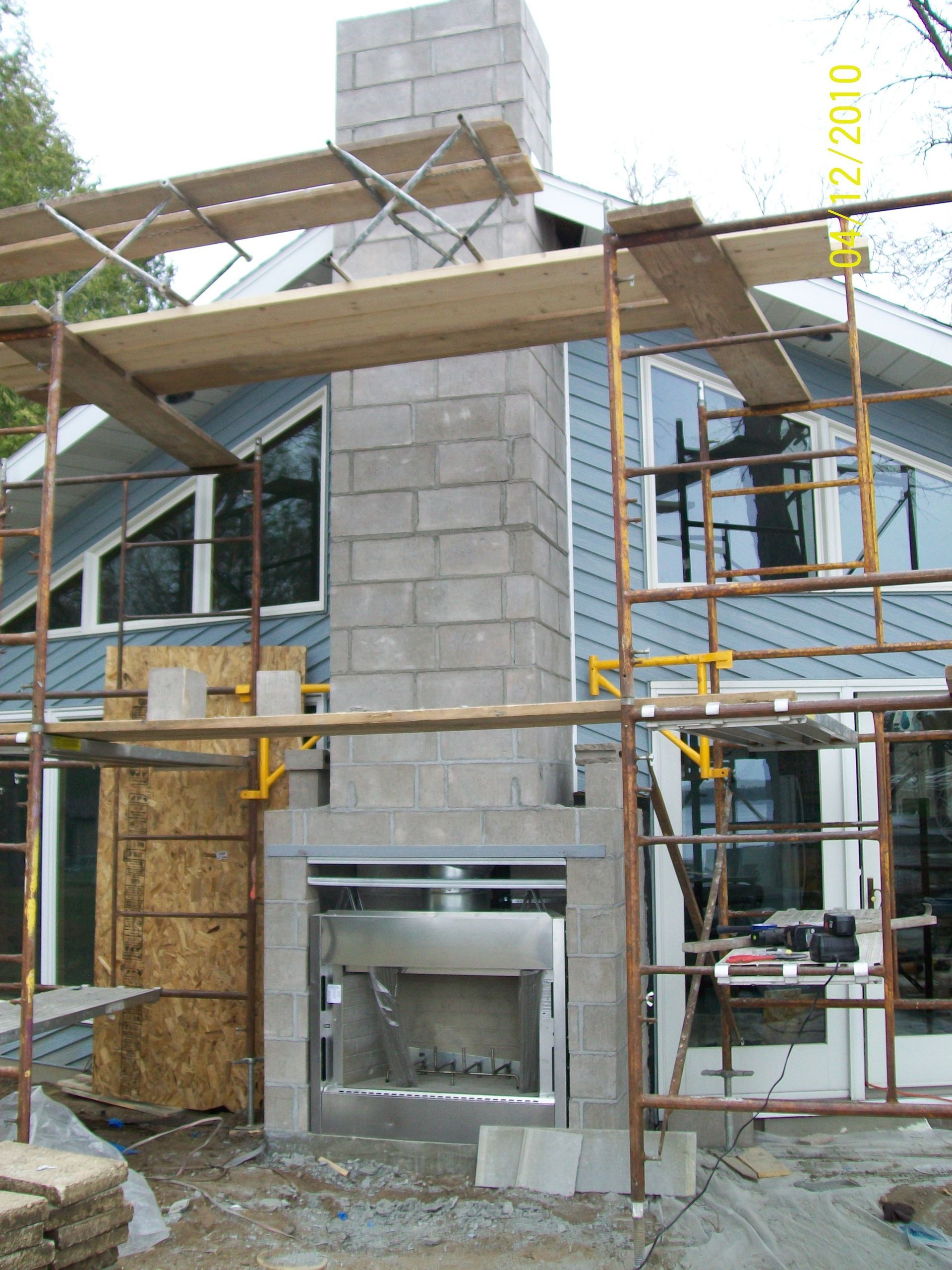 House under construction with scaffolding and unfinished stone chimney