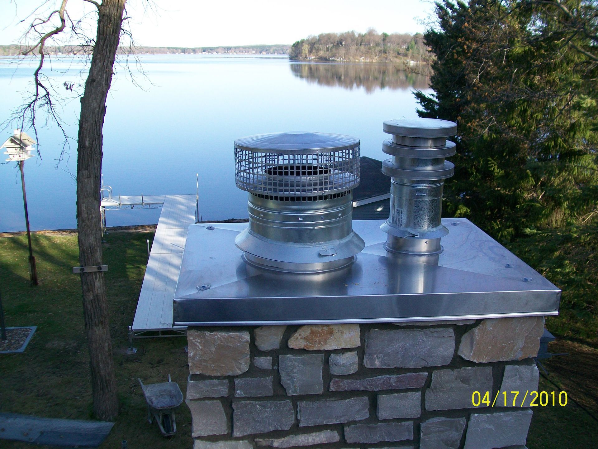 Rooftop vent pipes on a stone building beside a calm lake and trees