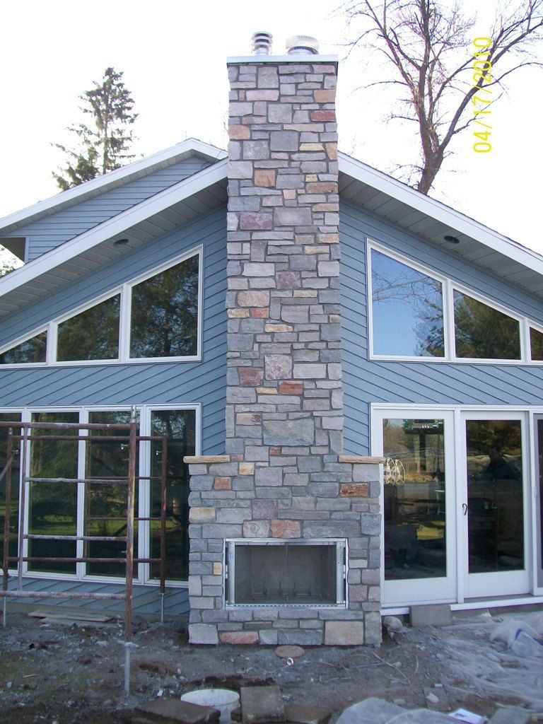 Stone chimney on a modern house exterior with blue siding and large windows under construction