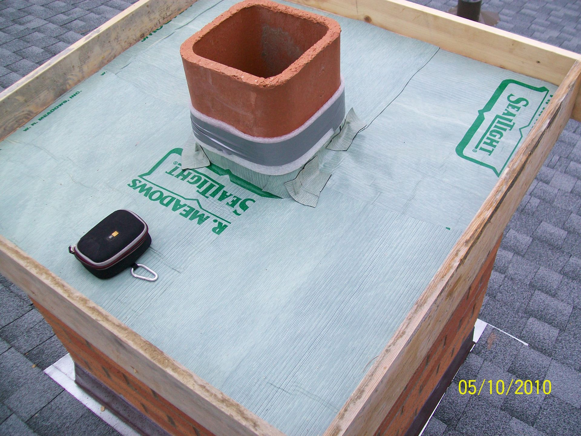 Insulated roof with a brick chimney vent, green labels, and a small black device on the surface