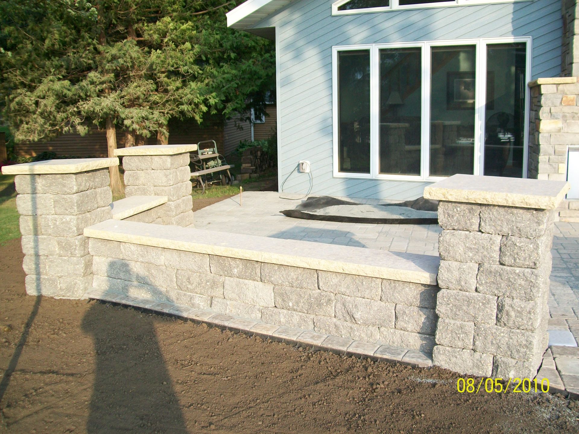 Stone patio with short walls and posts beside a house with white sliding glass doors.