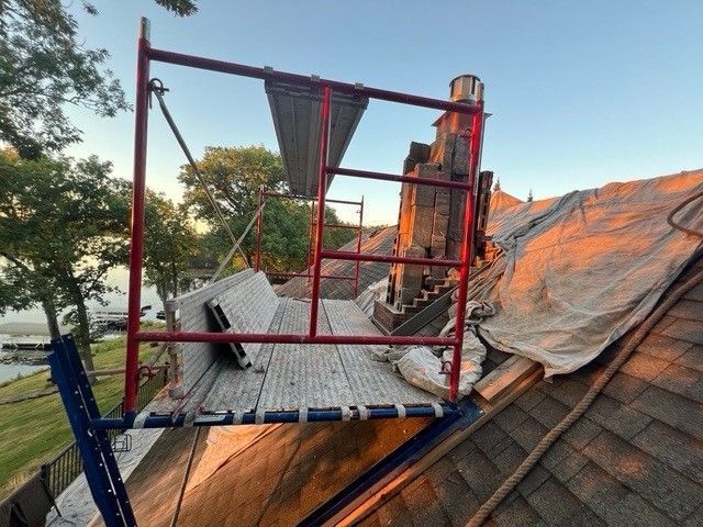 Scaffold on a roof beside a chimney, with torn roofing and tarps in an outdoor setting