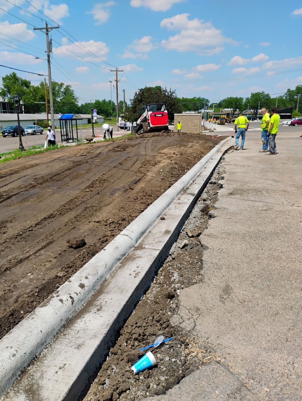 Road construction site with workers in safety vests, a red truck, and freshly graded dirt beside a curb
