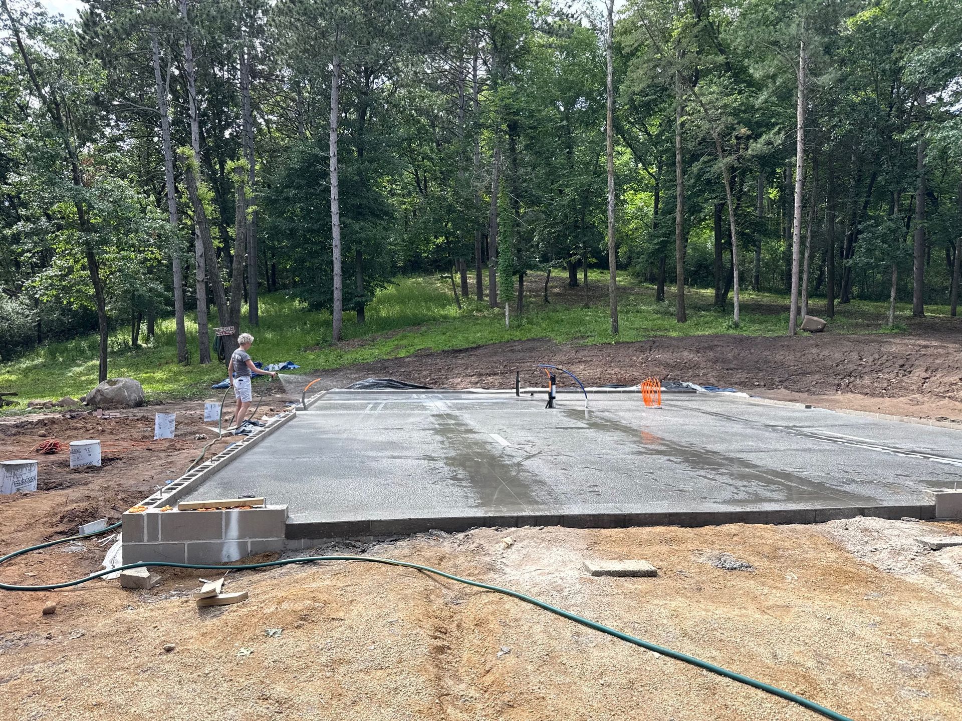 Fresh concrete foundation slab in a wooded construction site with scattered blocks and hoses