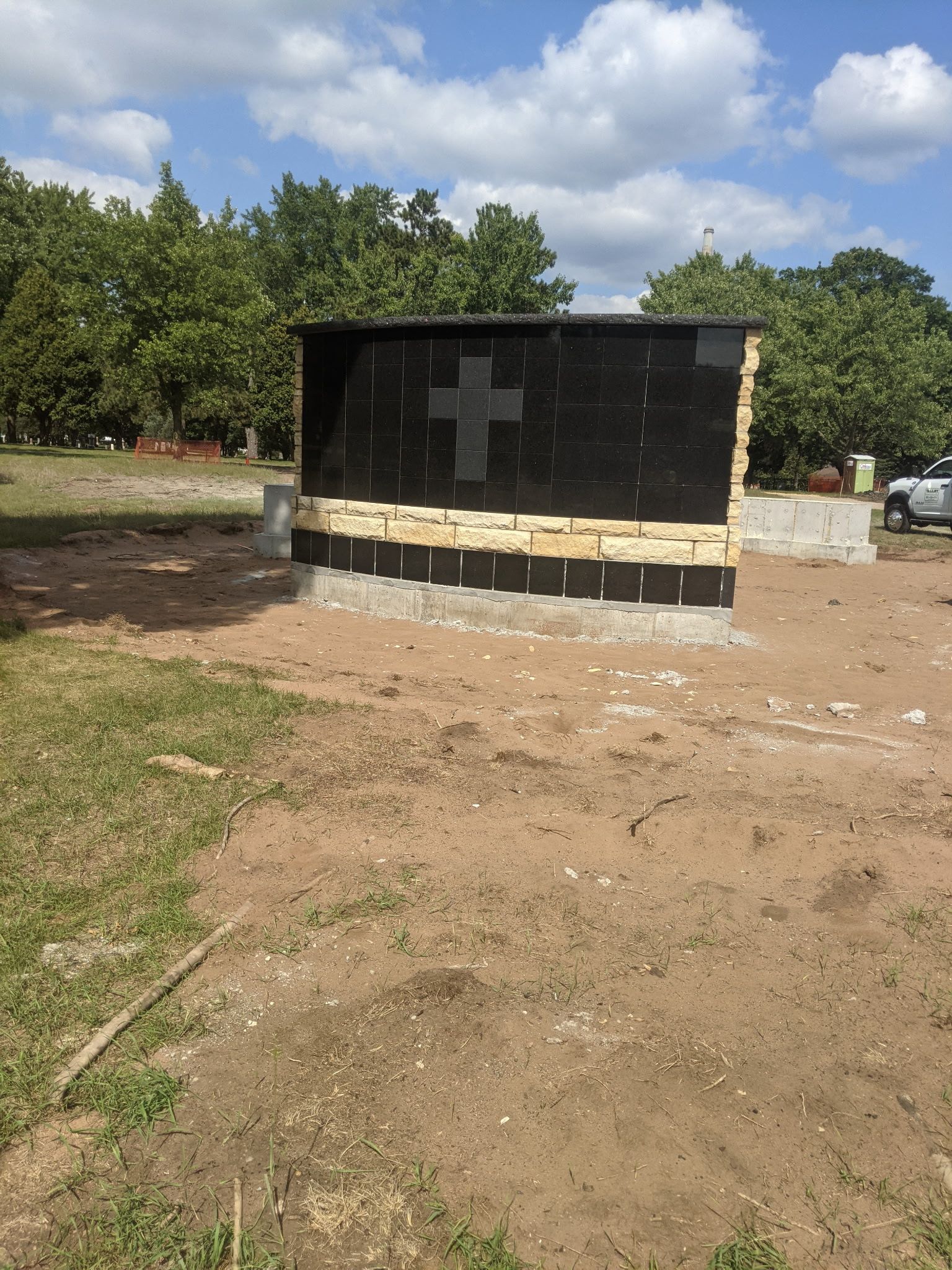 Black tomb with white cross in a sandy cemetery under a cloudy sky
