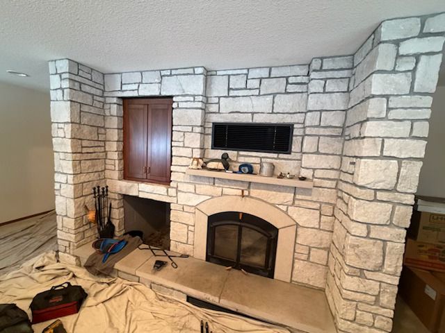 Stone fireplace wall with arched firebox, built-in TV niche, and tools on the floor in a living room