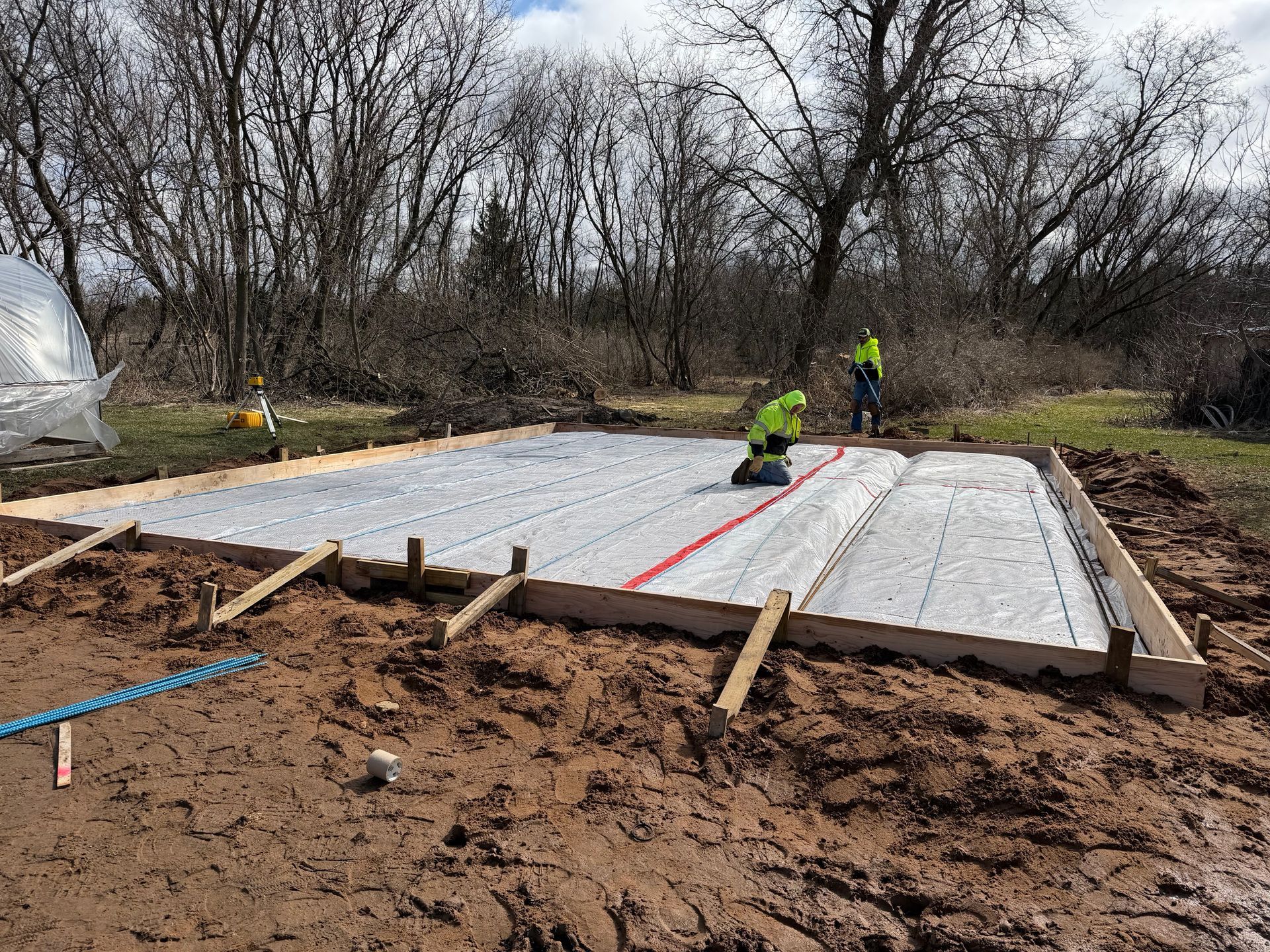 Foundation slab under construction on a muddy site, with workers and leveling lines visible.