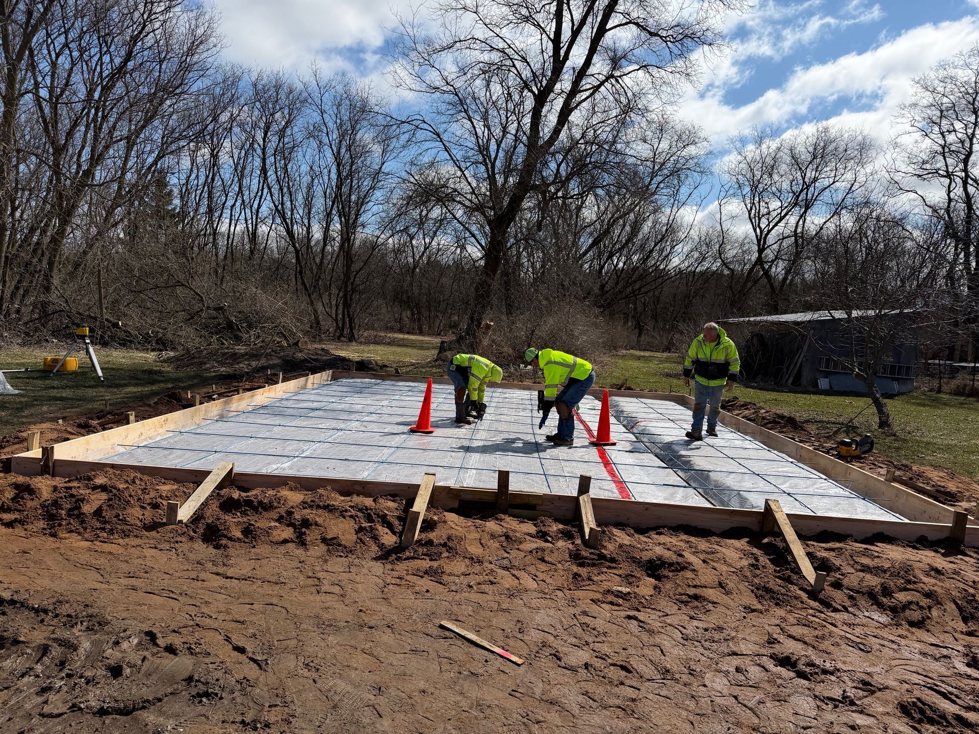 Workers in neon vests laying a concrete slab foundation at a muddy construction site