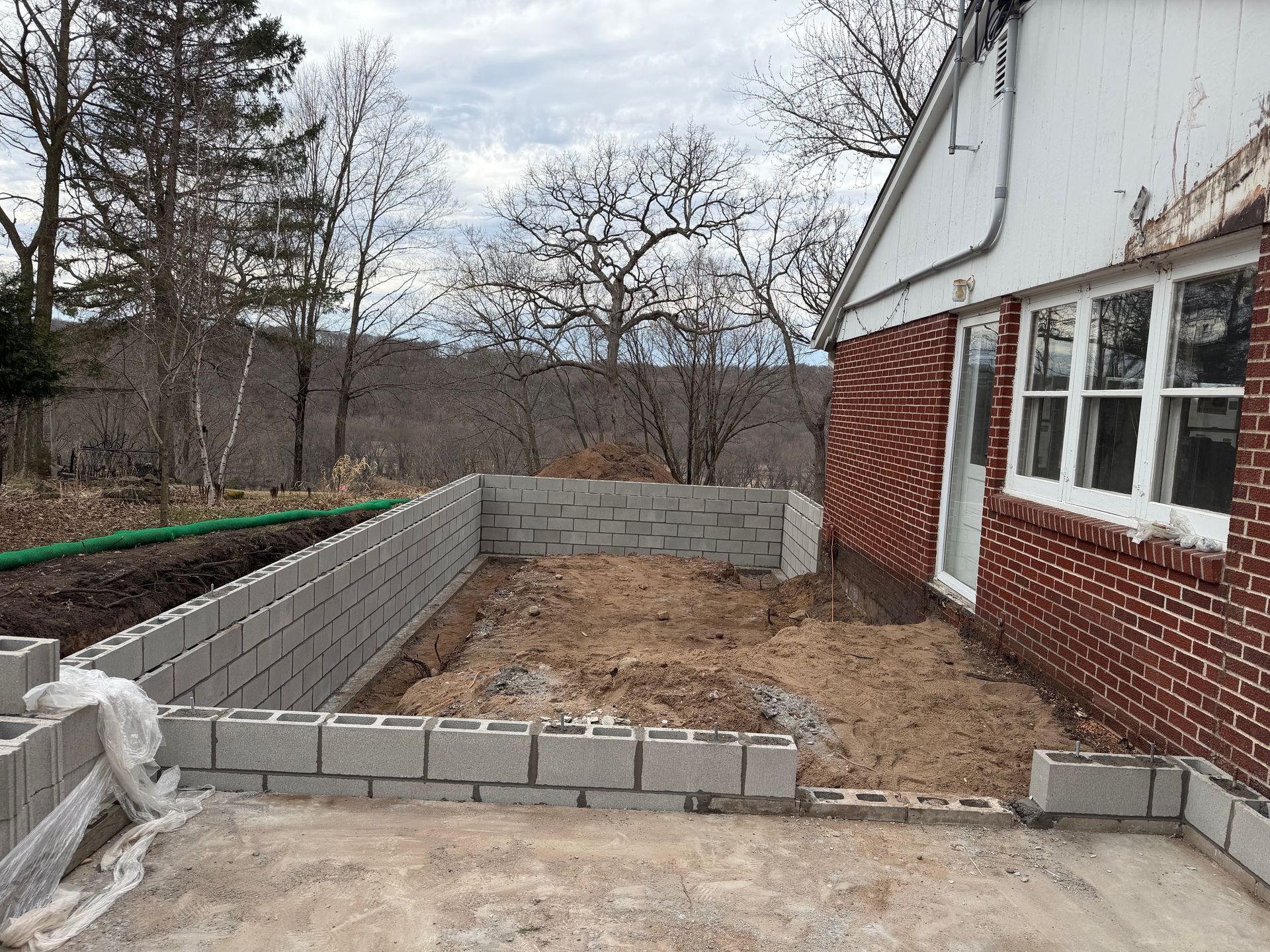 Partially built cinderblock foundation beside a white and red house in a bare yard