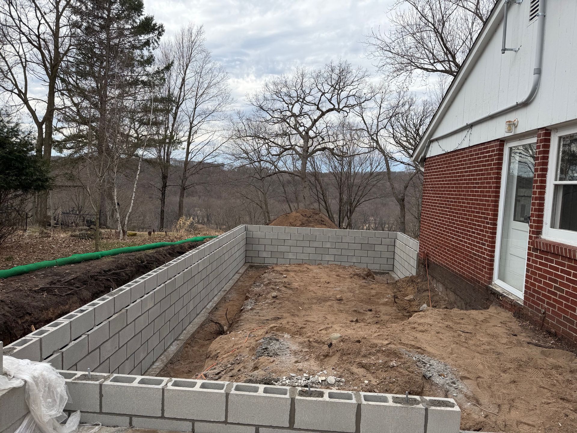 Partially built cinderblock retaining wall beside a brick house in a dirt yard
