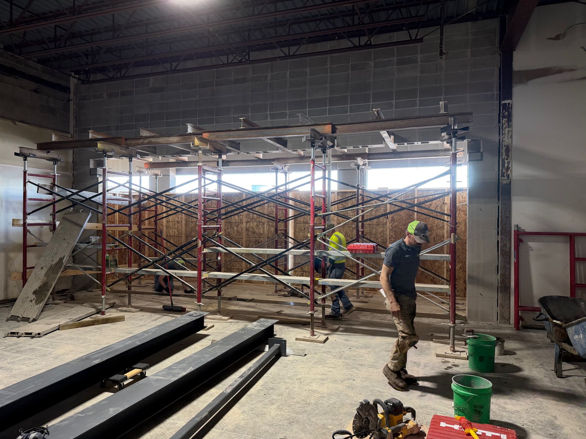 Construction workers under metal scaffolding inside an unfinished building with exposed walls and beams