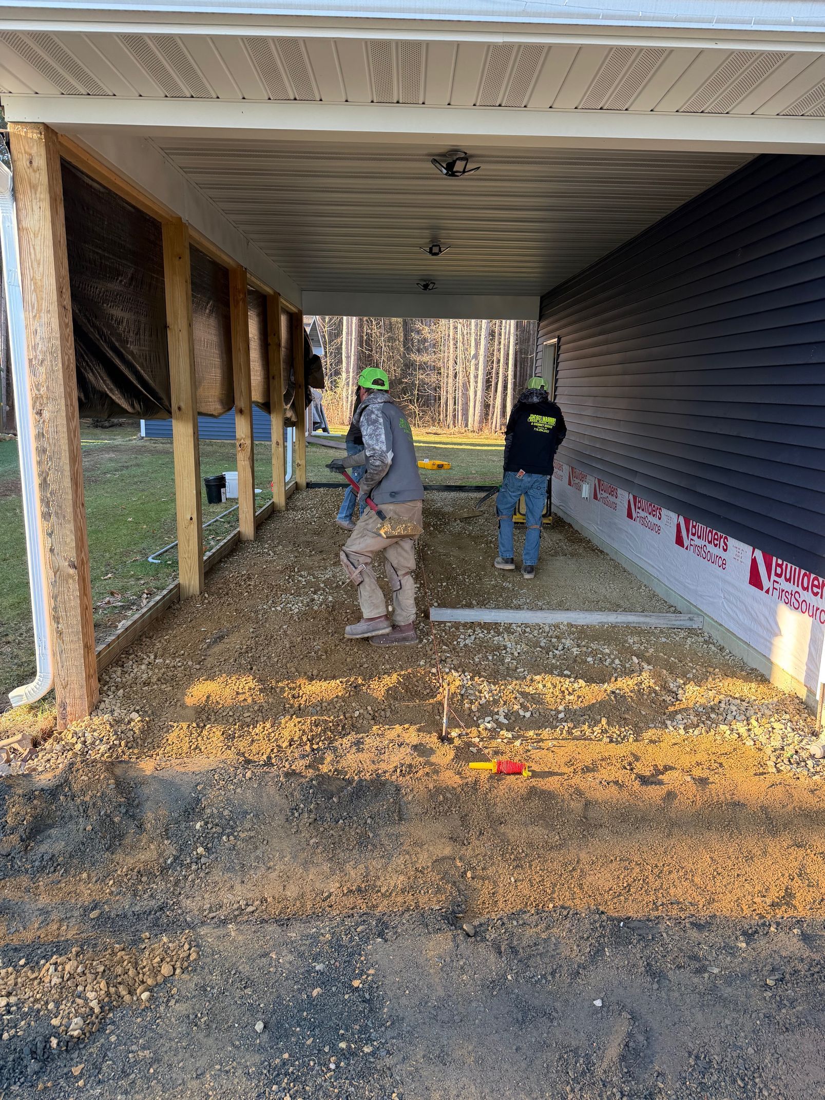 Construction workers inside a covered porch, installing insulation and materials under a house deck.