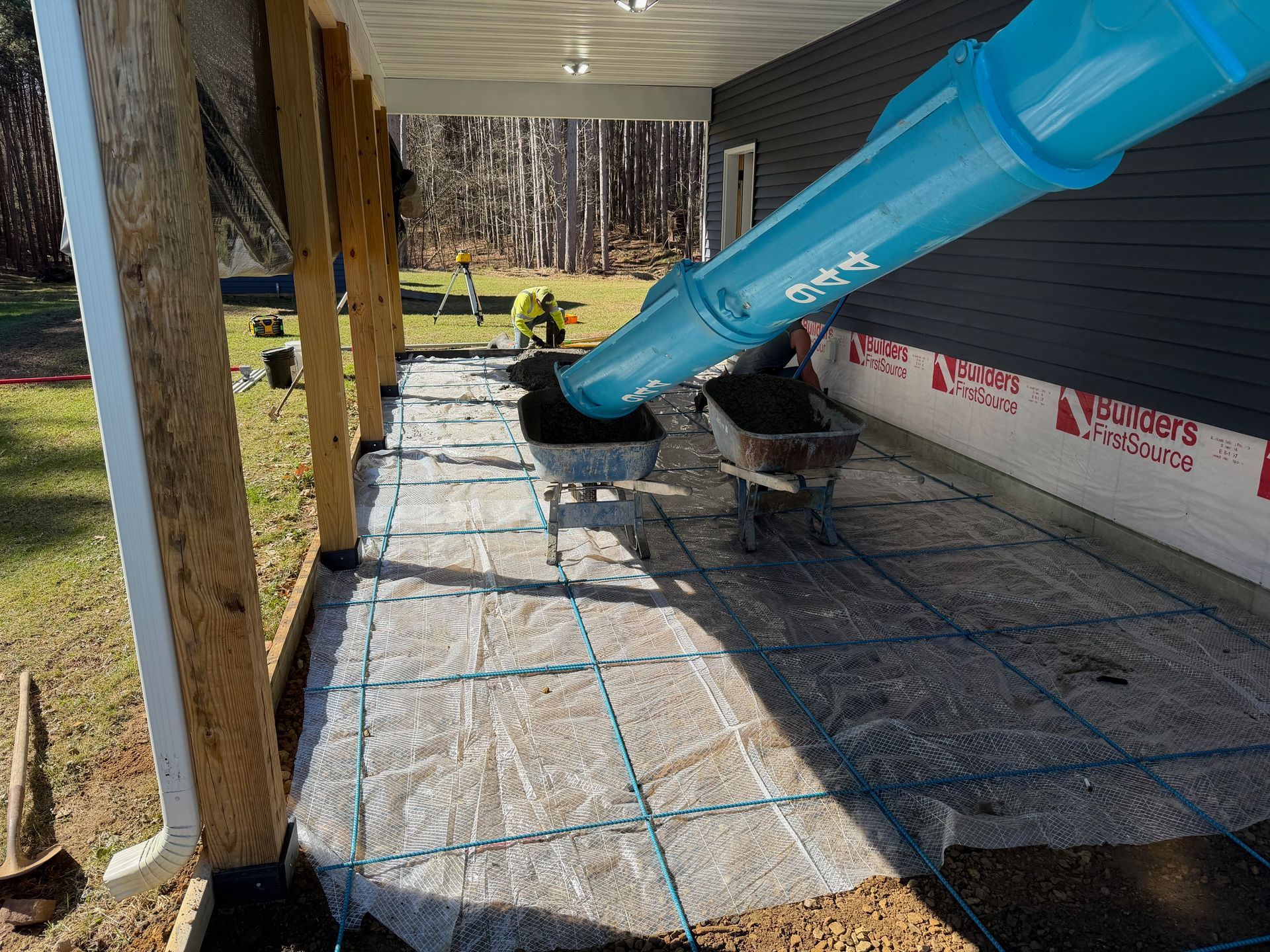 Blue slide chute over a house porch with workers installing roofing underlayment and plywood below.