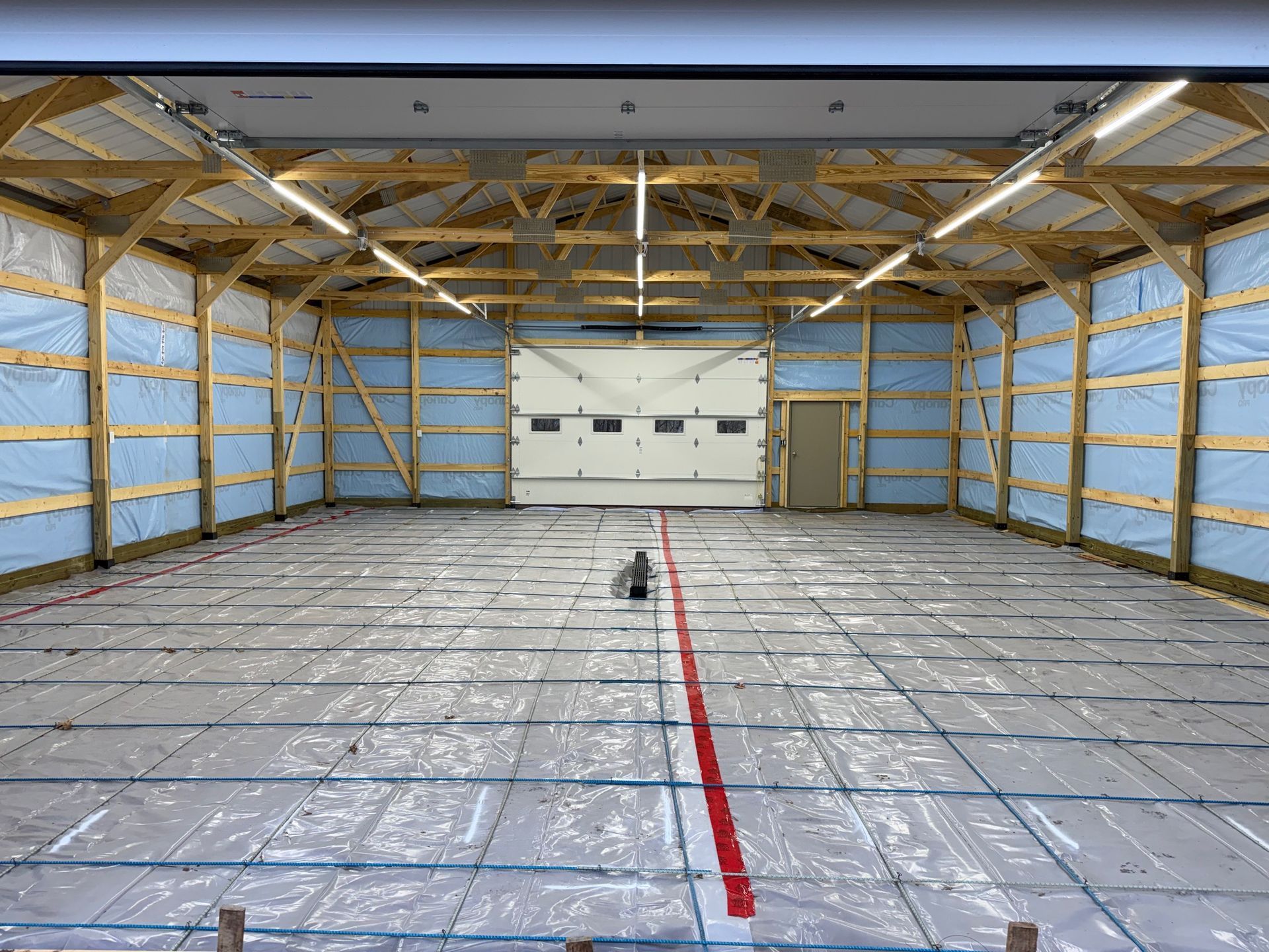 Empty garage interior with exposed framing, insulated walls, and plastic-covered floor with a red center line