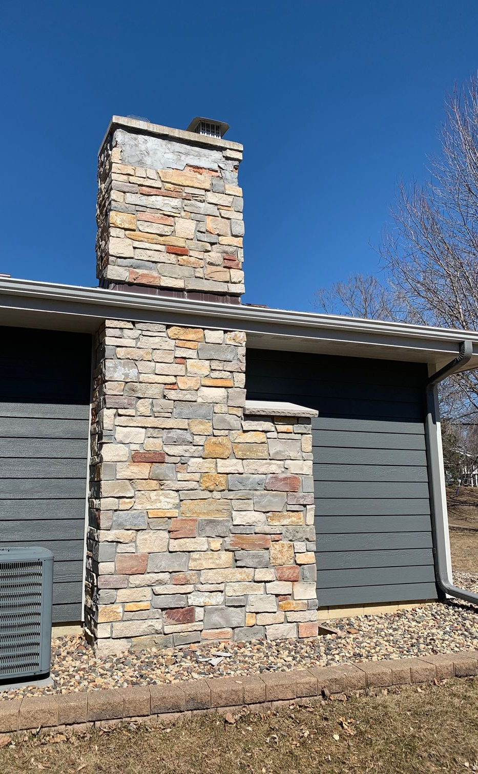 Stone chimney on a gray-sided house under a clear blue sky.