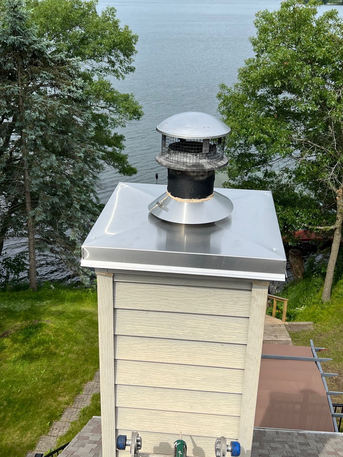 Rooftop vent on a small cream-colored building overlooking a lake, framed by trees