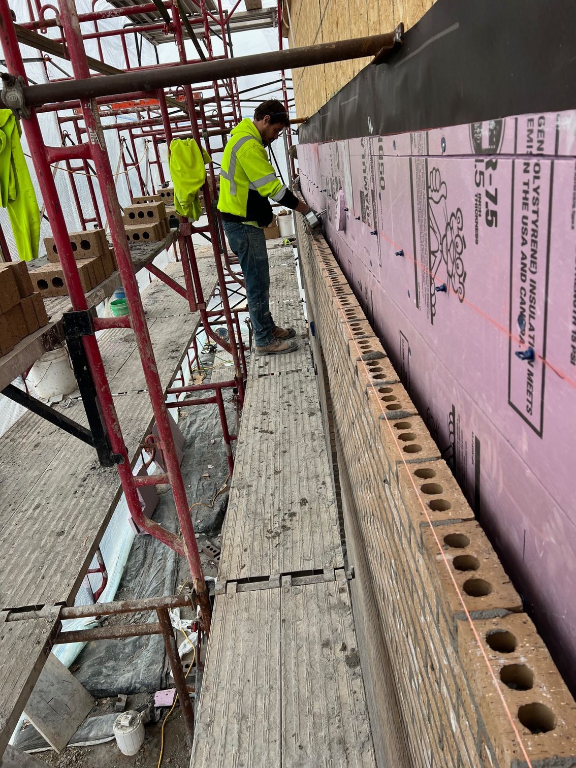 Construction worker on scaffolding beside pink wall insulation panels at an outdoor building site