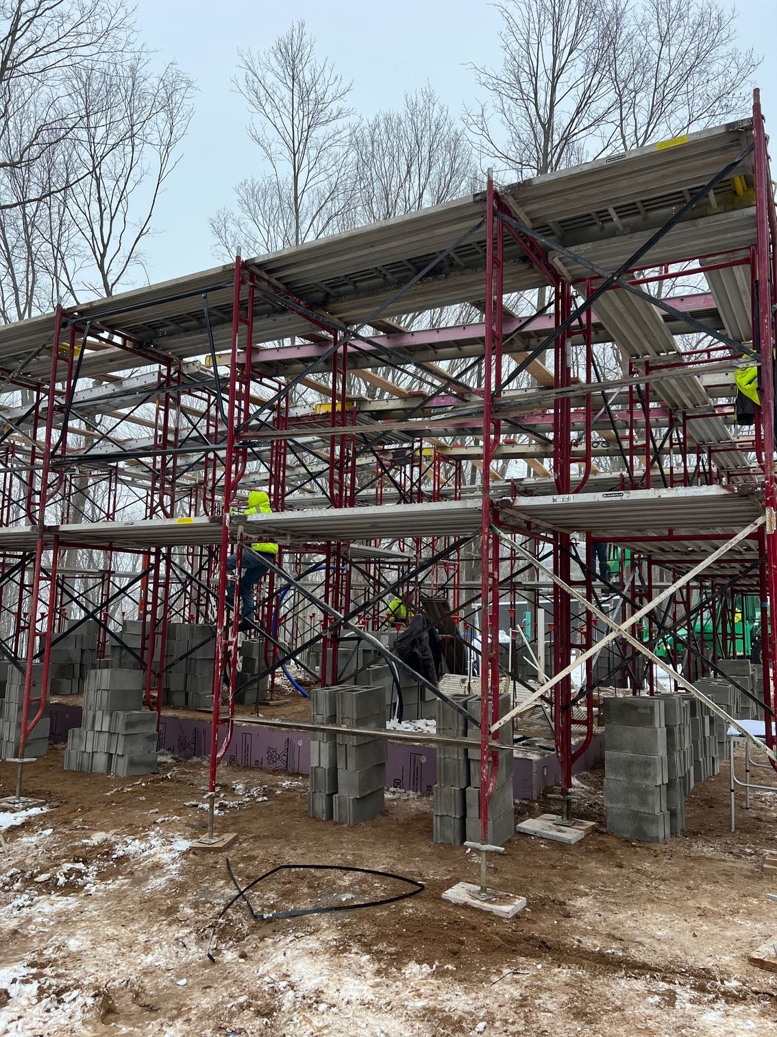 Partially built scaffolded structure with workers, red metal supports, and snow on the ground