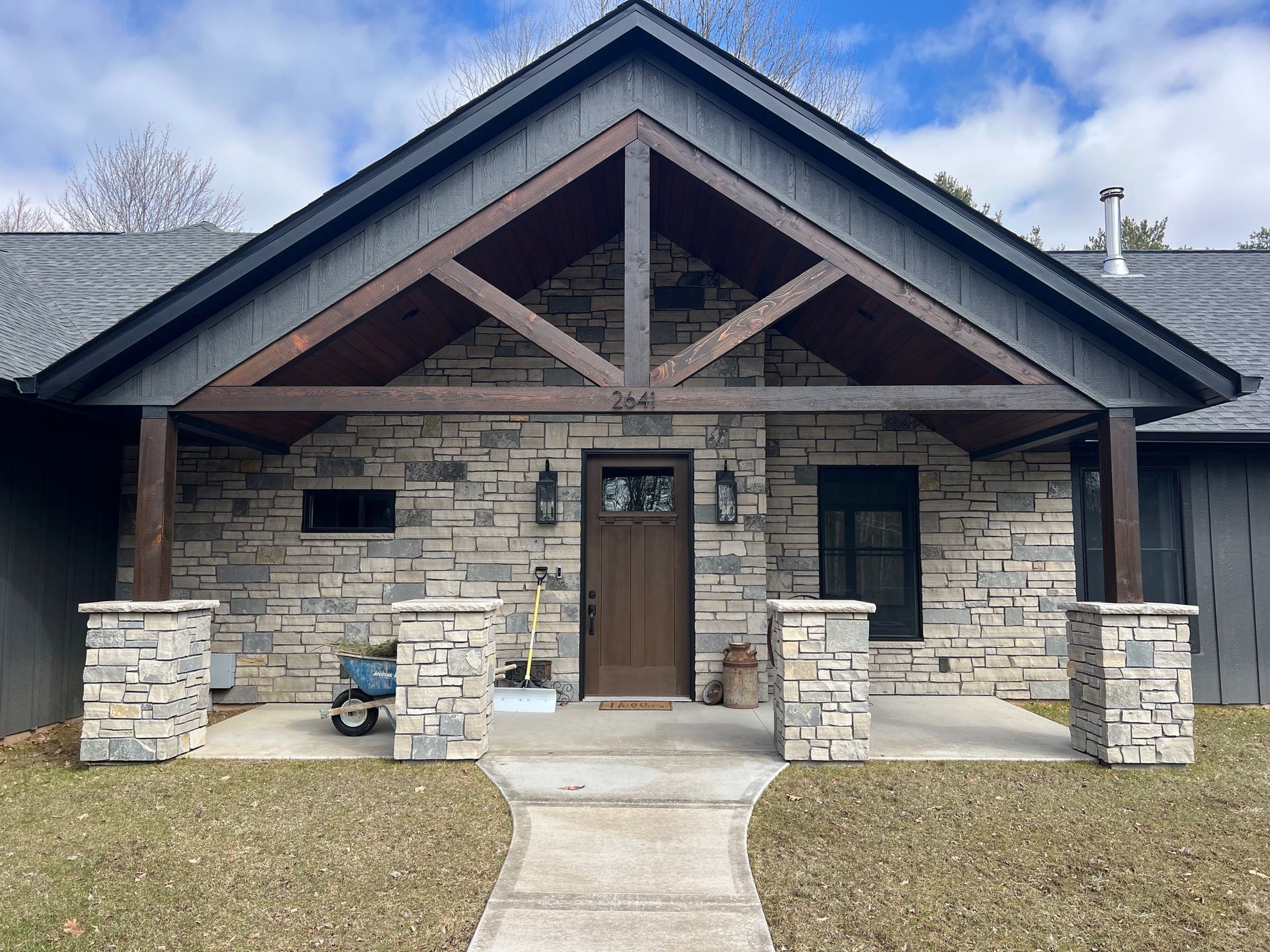 Front porch of a stone house with wood beams, a centered wooden door, and two small front windows.