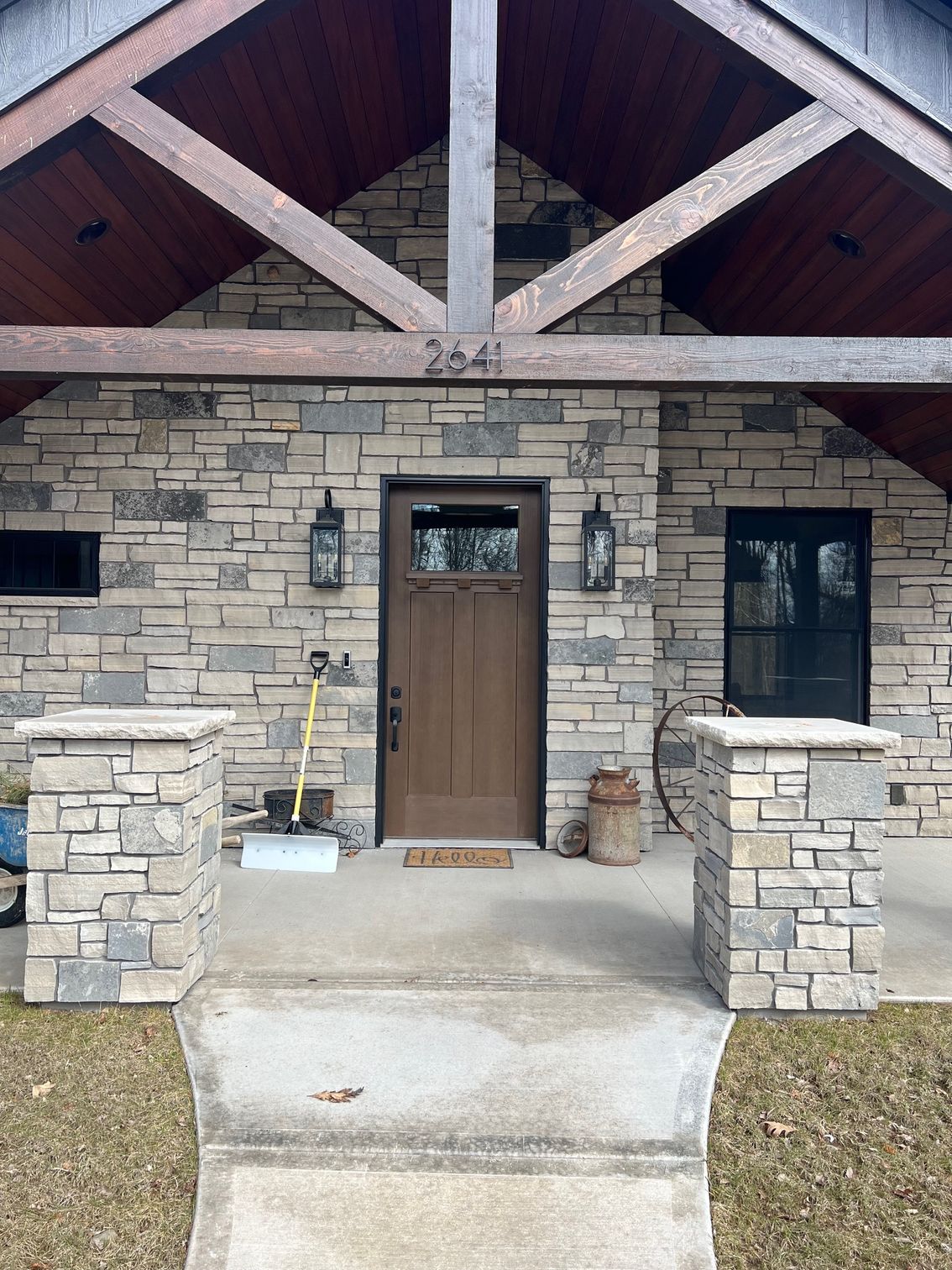 Stone-front house entry with wood door, black lanterns, and covered porch with exposed beams