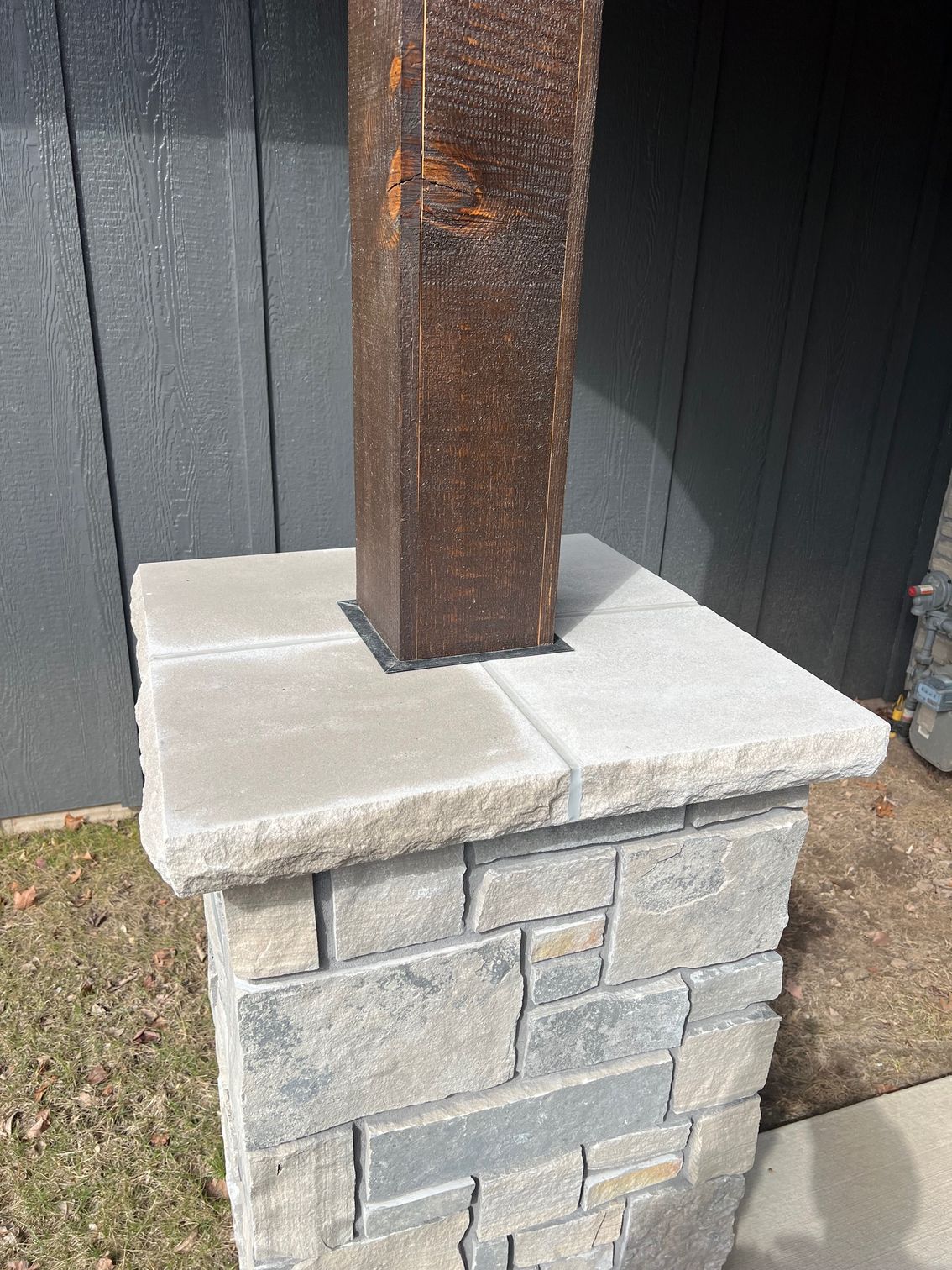 Rusty metal post mounted on a stone pillar beside a dark wooden fence.