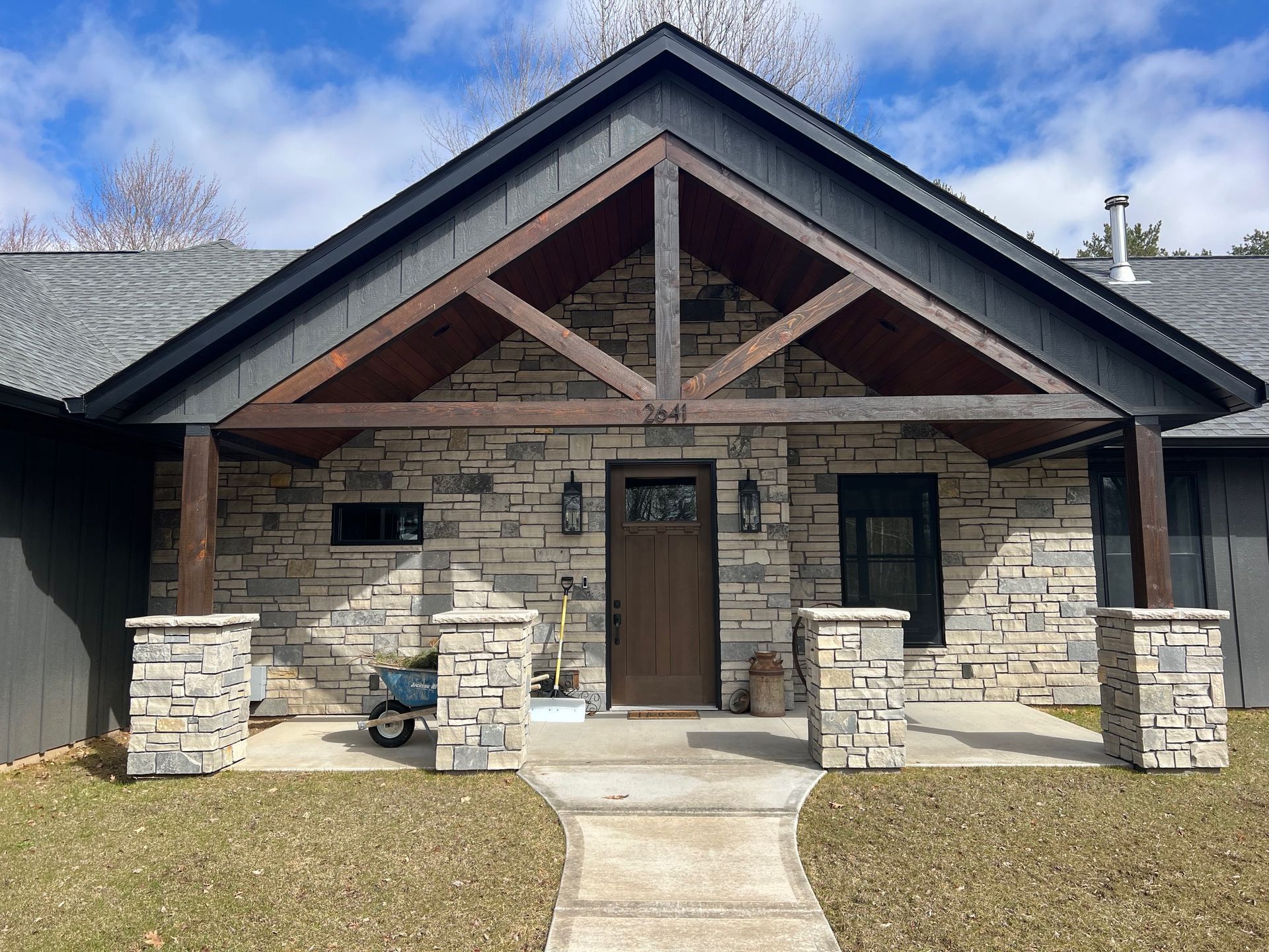 Front view of a stone house with a gabled roof, wooden porch beams, and a central front door