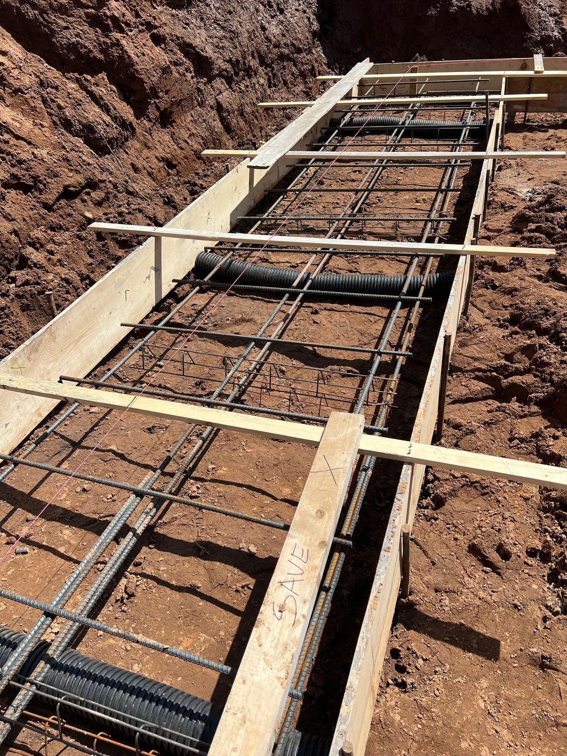 Rebar grid and wooden formwork for a concrete foundation trench at a construction site