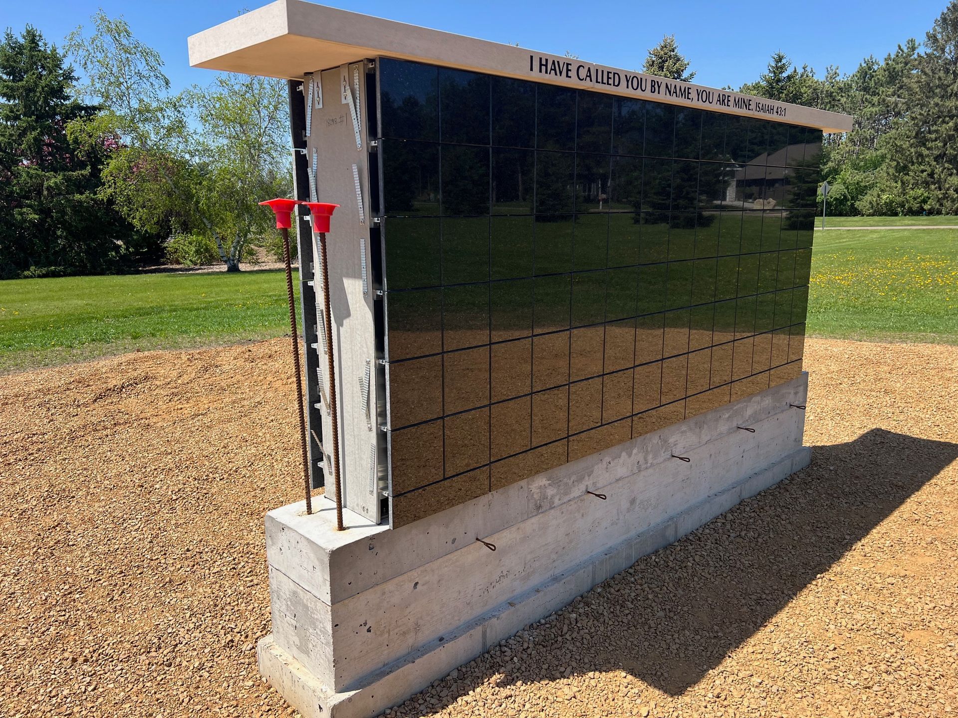 Outdoor utility cabinet with reflective dark panels on a concrete base beside a grassy field.