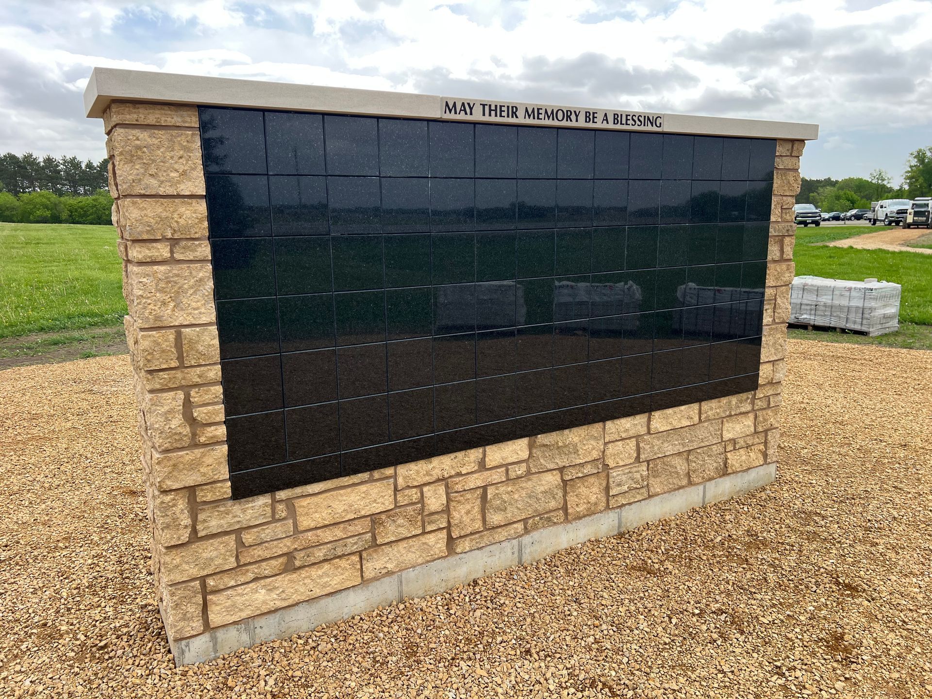 Outdoor memorial wall with dark plaques and tan stone base in a grassy field