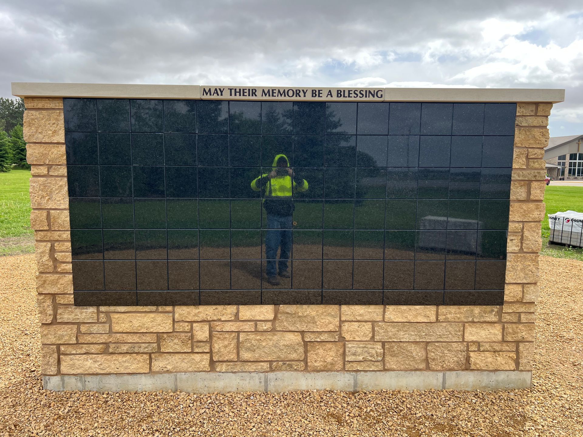 Stone memorial wall with dark plaques reflecting a person in a neon shirt