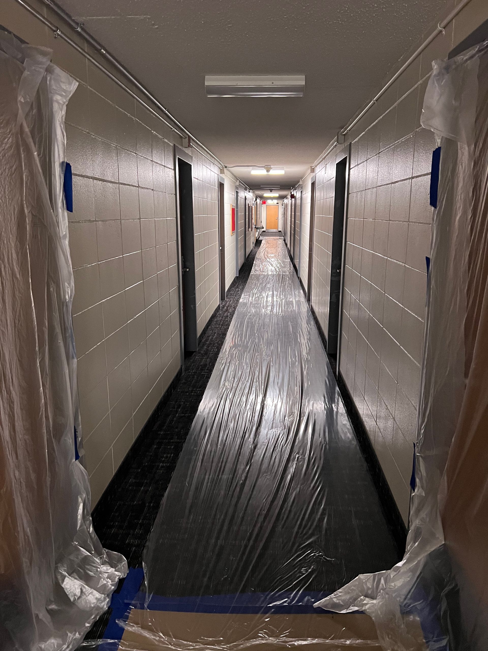 Narrow hallway under renovation, wrapped in protective plastic with covered floor and walls.