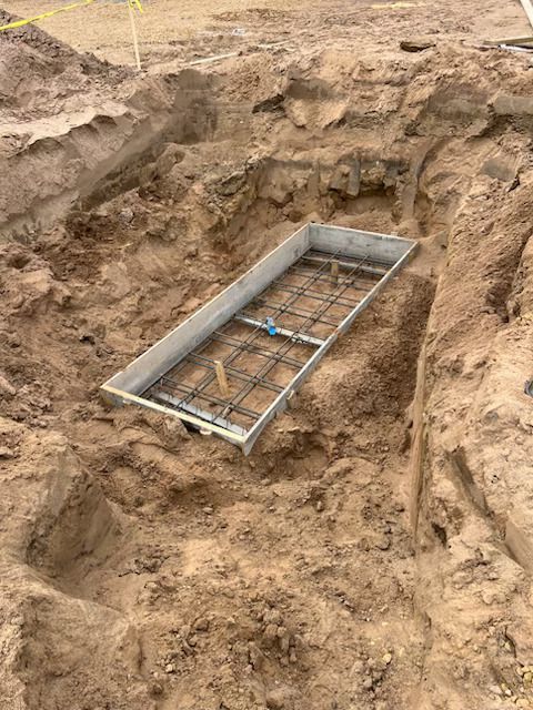 Shallow dirt trench with a rectangular concrete form and rebar in the center of an excavation site