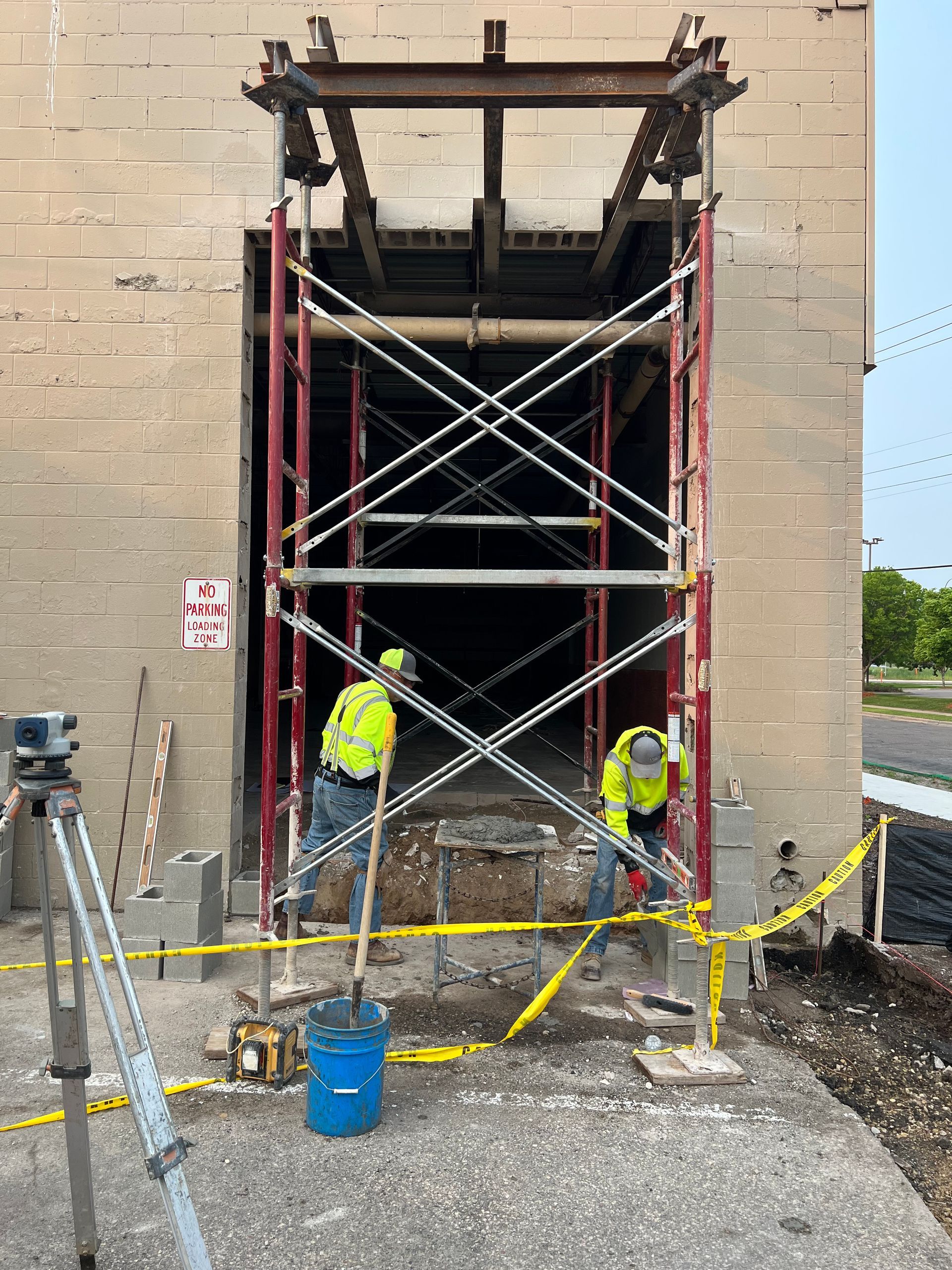 Construction workers on scaffolding repairing a building wall beside caution tape and equipment