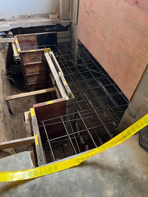 Construction site with exposed rebar, wooden formwork, and yellow caution tape around an opening