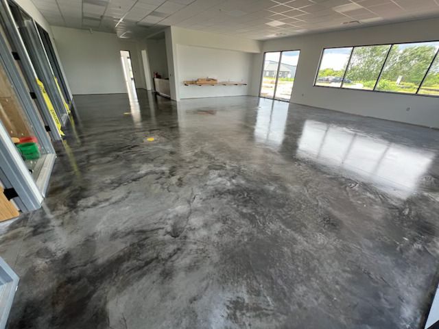 Empty room with glossy gray concrete floor, windows on right, and ladders leaning against the left wall
