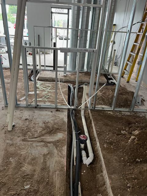 Interior construction site with exposed wall studs, floor trench, and plumbing pipes.