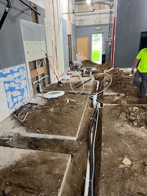 Construction site hallway with trenching, exposed pipes, and debris beside unfinished walls