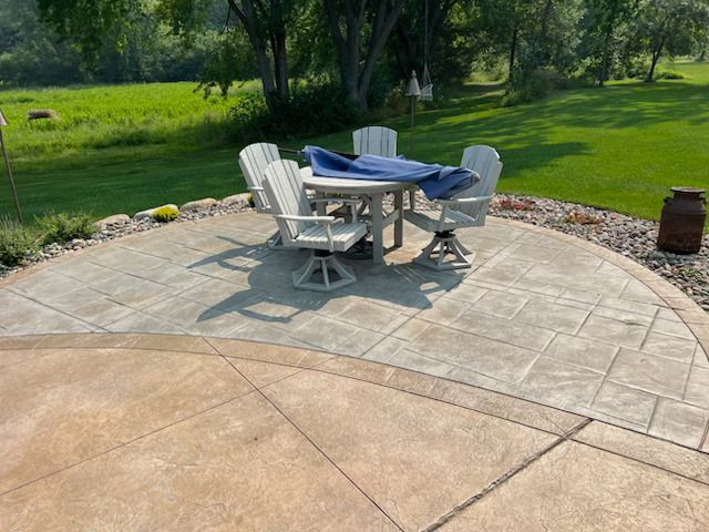 Patio with round table and chairs on a stone terrace beside a green lawn and trees