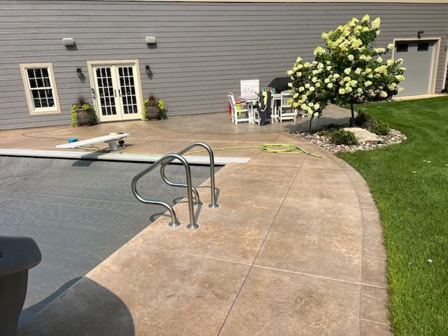 Backyard pool deck with metal handrails, stone patio, green lawn, and house doors in the background