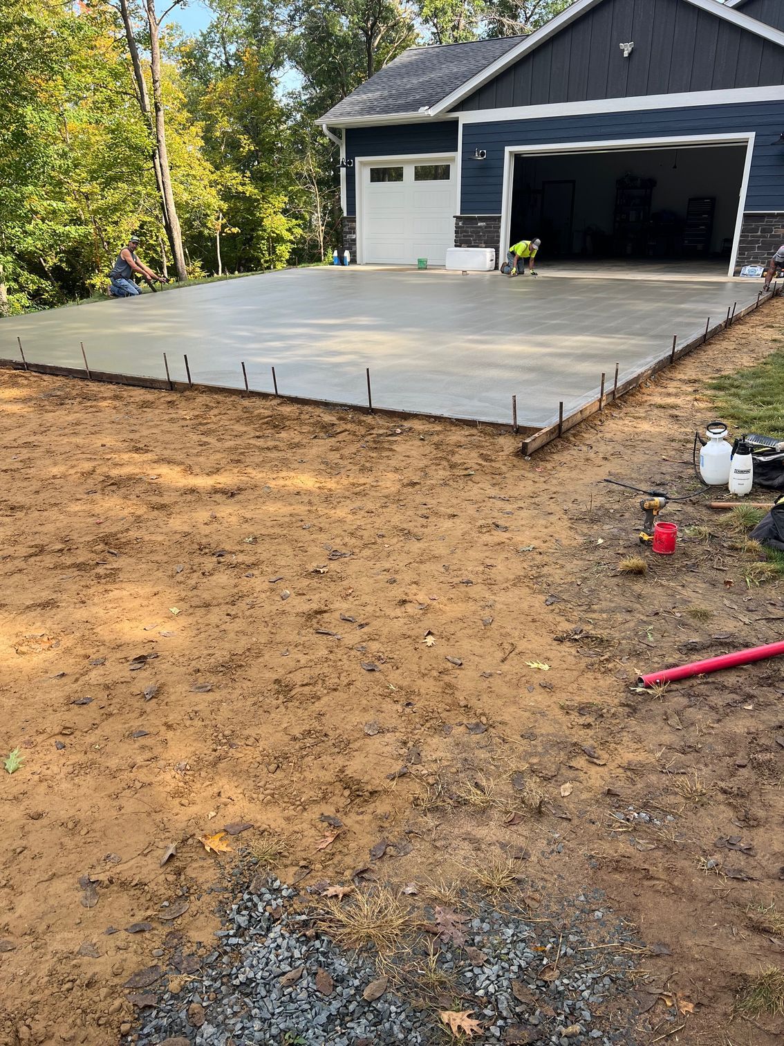 Concrete driveway slab being poured in front of a garage, with dirt and gravel in the foreground.
