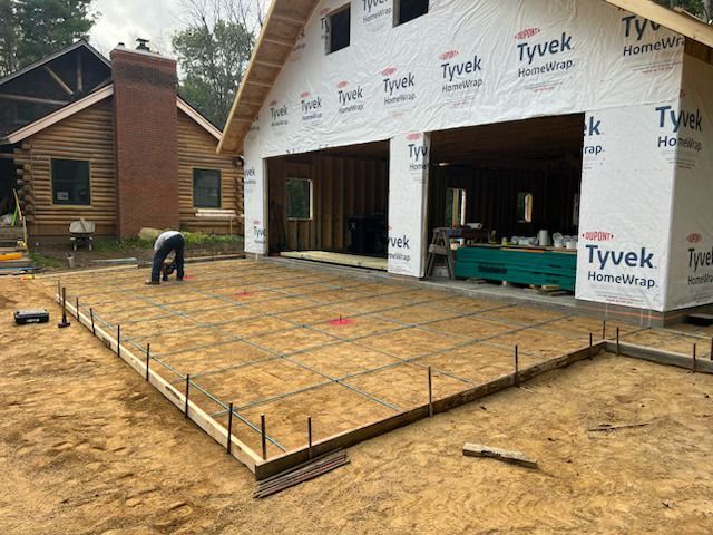 House under construction with Tyvek wrap and a worker leveling a wooden foundation frame