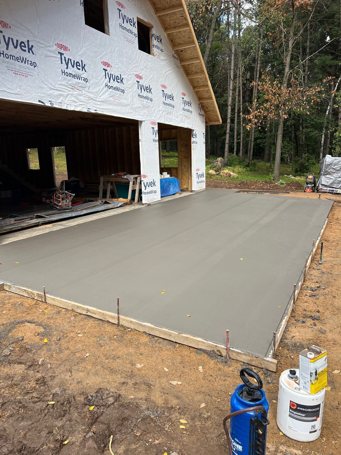 Freshly poured concrete slab beside a house under construction, with tools and lumber nearby.