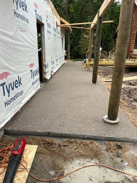 Exterior home renovation with Tyvek-wrapped wall, gravel path, and wooden posts supporting a raised deck